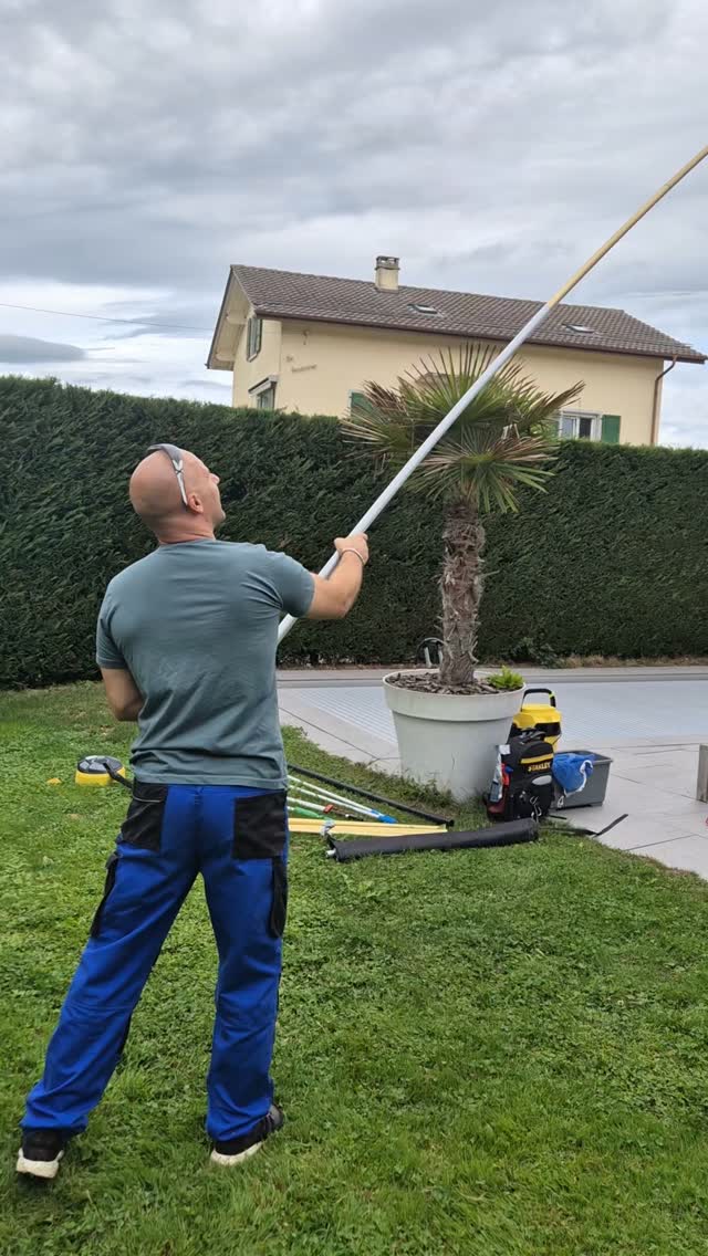 Un technicien Aplus nettoie une fenêtre à l'aide d'une perche, façade moderne baignée de soleil